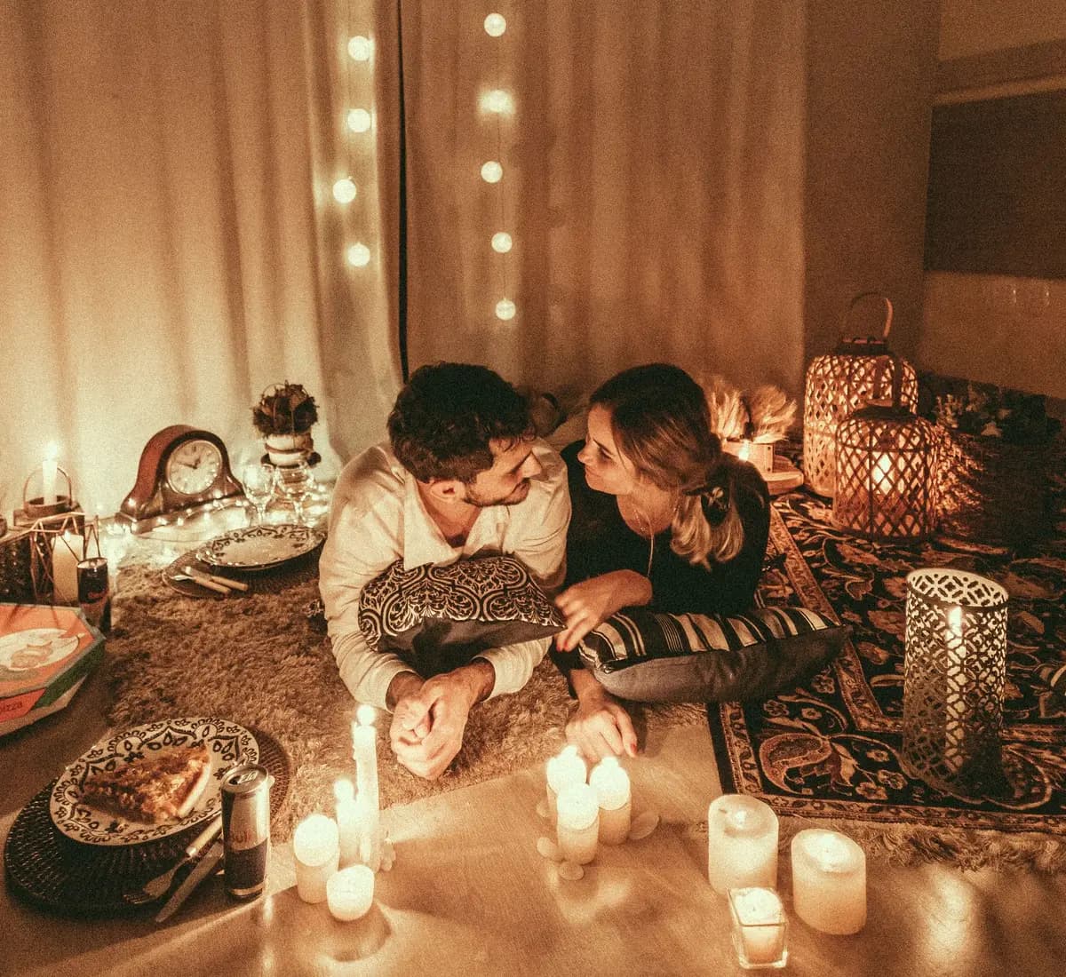 A couple lying on a rug at home, lit by candles and string lights