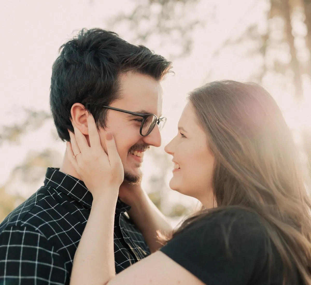 A couple outdoors at golden hour, her hand on his cheek, both laughing